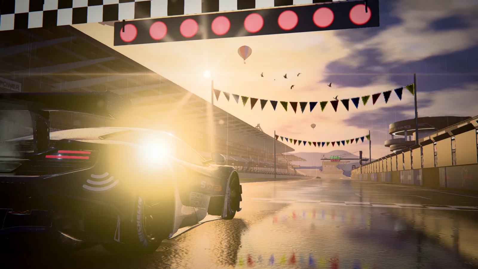 A GT3 race car on the starting grid, under a checkered banner and a row of red start lights, with the low sun flaring over the pit straight