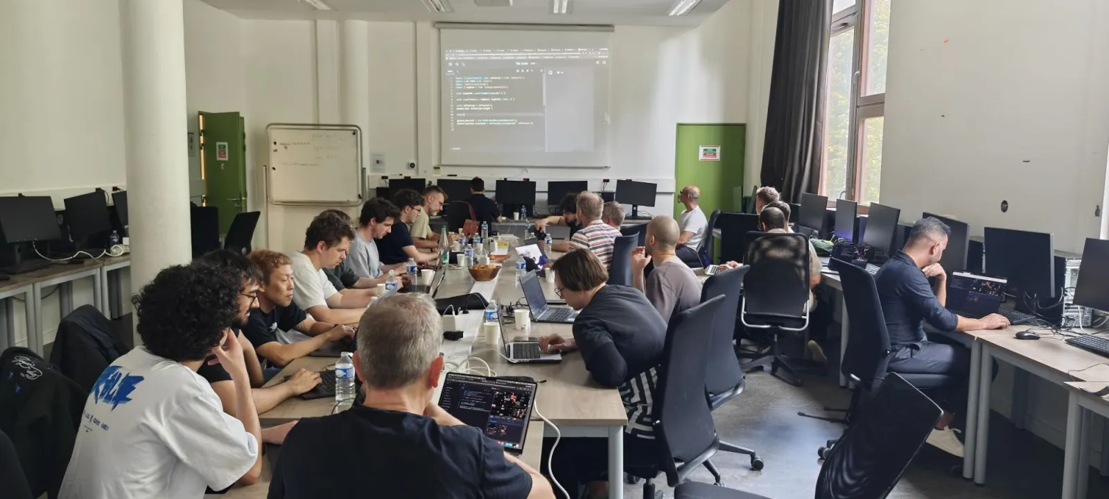The workshop room, with participants at a long table and TSL code on the projector